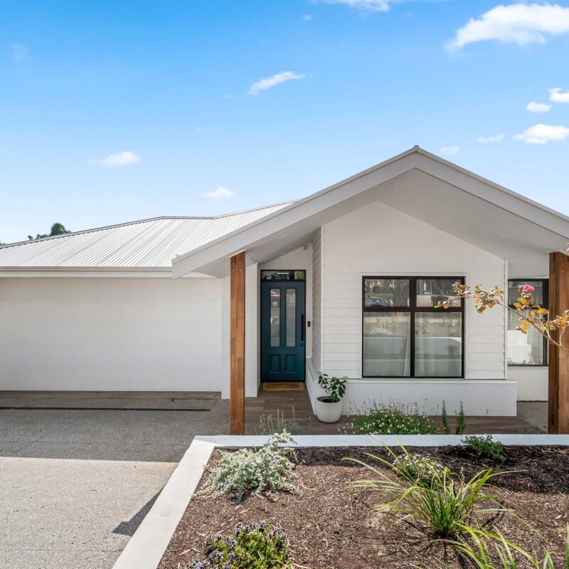 Single-storey coastal home in South Brighton Adelaide with white weatherboard facade, gabled roof and timber posts.