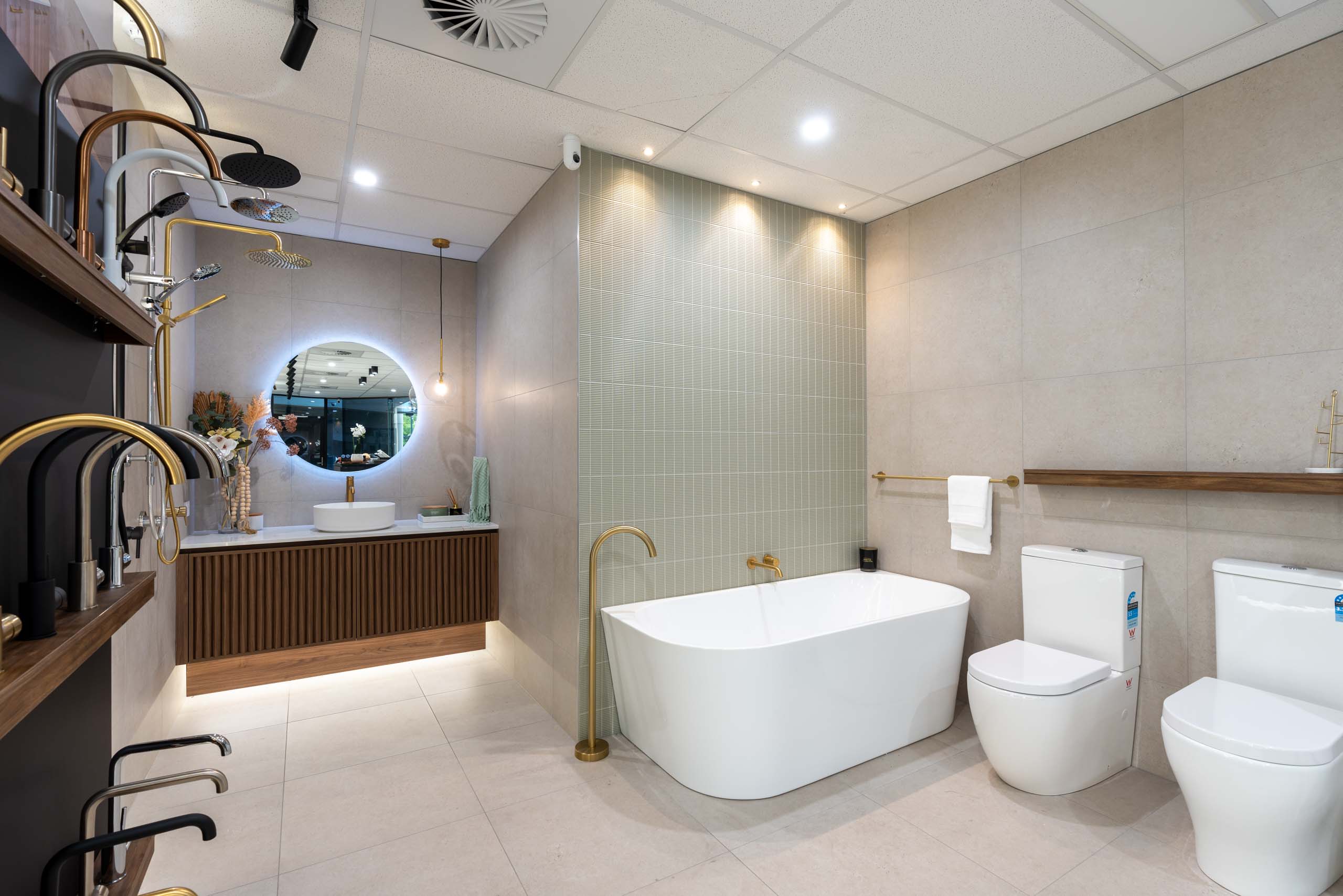 Inside the My Home Build My Style Studio selection centre in Adelaide, showing modern bathroom displays with a freestanding bathtub, textured green feature tiles, brushed brass tapware, and a fluted timber vanity under an LED backlit mirror.