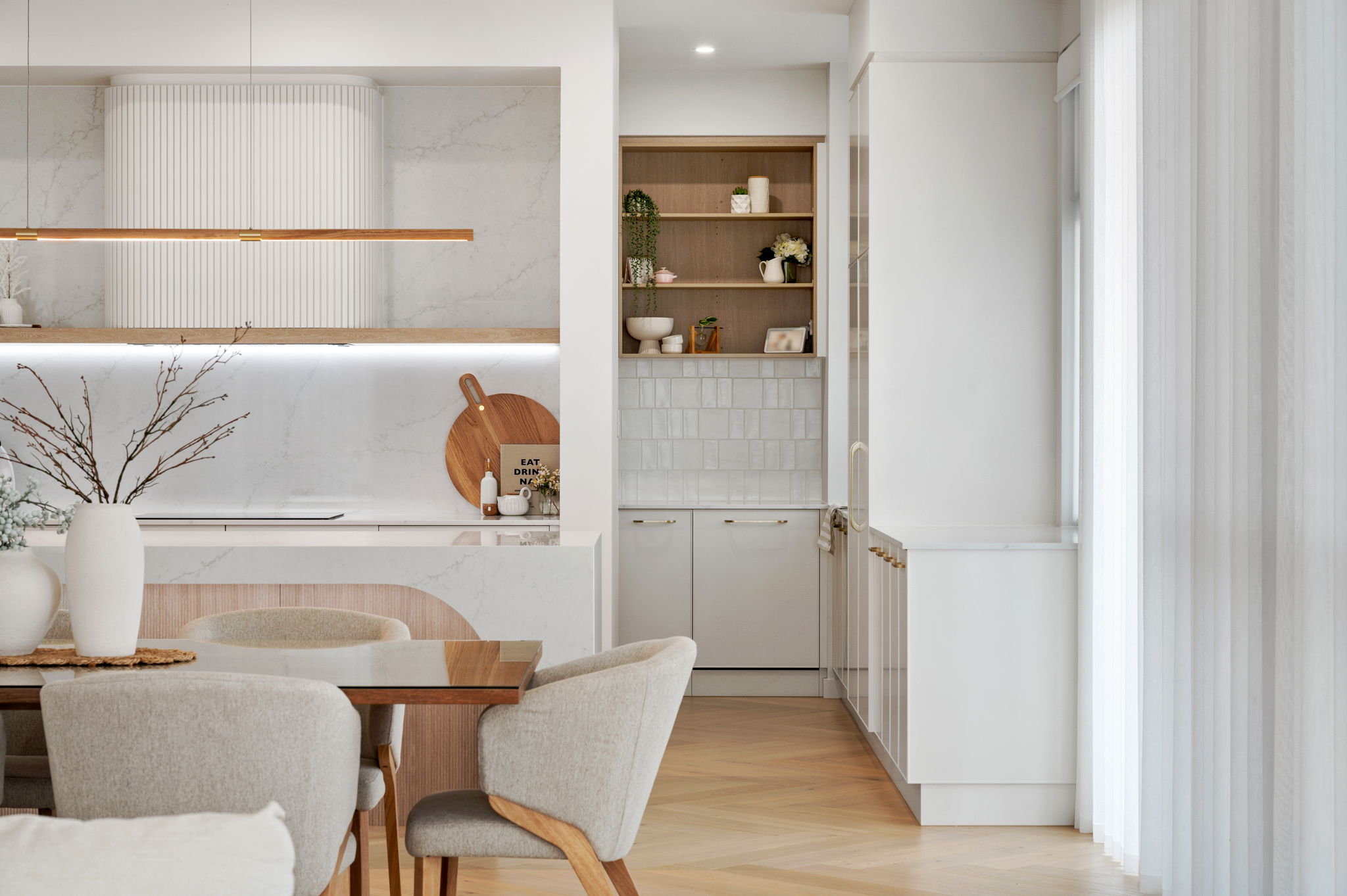 Custom kitchen and butler pantry joinery featuring white marble look benchtops, warm timber accents, a curved island bench, and custom white cabinetry in an open-plan Adelaide home design.